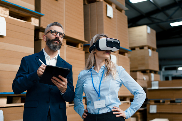 Warehouse managers talking logistics using VR, controlling stock levels, discussing shipping process. Virtual reality in inventory management. Smart glasses guiding female manager through warehouse, recording tracking data and quicken picking process.