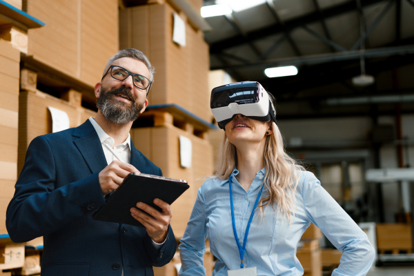 Warehouse managers talking logistics using VR, controlling stock levels, discussing shipping process. Virtual reality in inventory management. Smart glasses guiding female manager through warehouse, recording tracking data and quicken picking process.