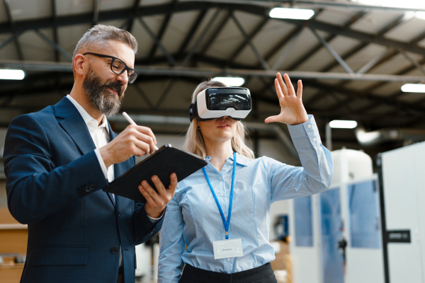 Engineers talking project using VR, in modern industrial factory. Virtual reality and technology in manufacturing industry, Smart glasses guiding female and male manager through process and planing.