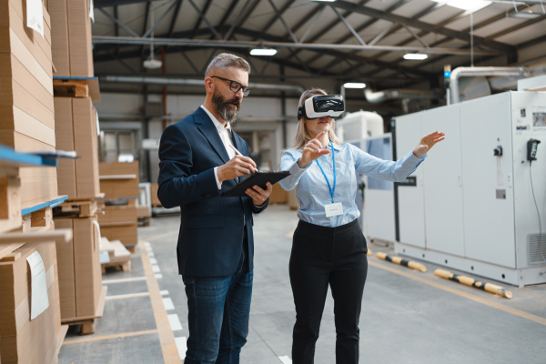 Warehouse managers talking logistics using VR, controlling stock levels, discussing shipping process. Virtual reality in inventory management. Smart glasses guiding female manager through warehouse, recording tracking data and quicken picking process.