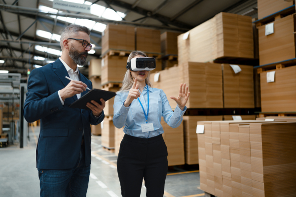 Warehouse managers talking logistics using VR, controlling stock levels, discussing shipping process. Virtual reality in inventory management. Smart glasses guiding female manager through warehouse, recording tracking data and quicken picking process.