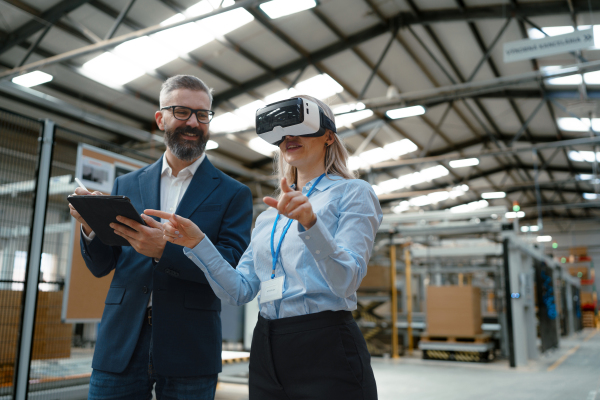 Engineers talking project using VR, in modern industrial factory. Virtual reality and technology in manufacturing industry, Smart glasses guiding female and male manager through process and planing.