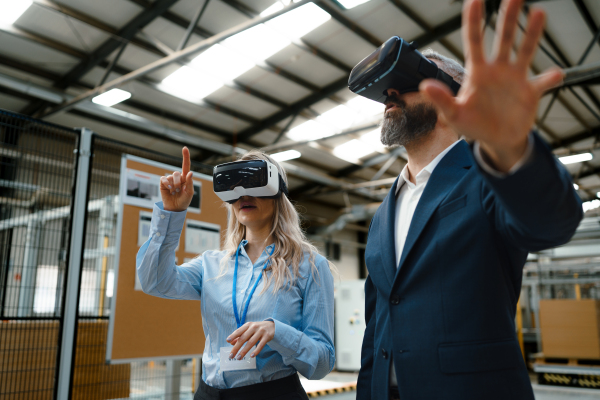 Engineers talking project using VR, in modern industrial factory. Virtual reality and technology in manufacturing industry, Smart glasses guiding female and male manager through process and planing.