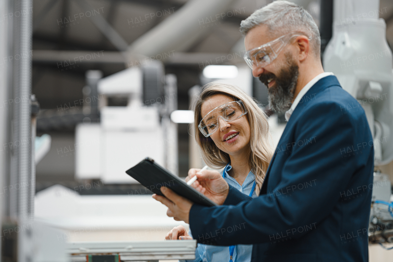 Female engineer and male production manager standing in modern industrial factory, talking about production. Manufacturing facility with robotics, robotic arms and automation.