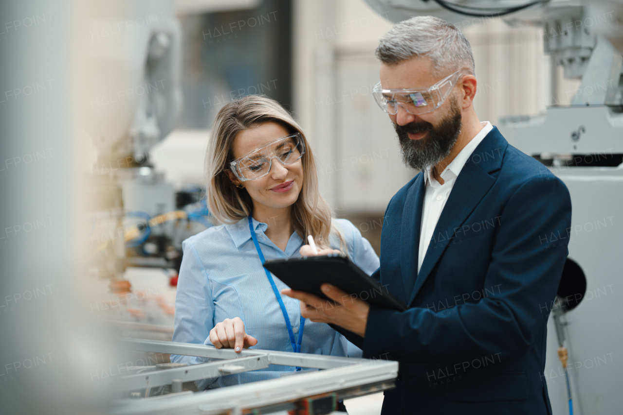 Female engineer and male production manager standing in modern industrial factory, talking about production. Manufacturing facility with robotics, robotic arms and automation.