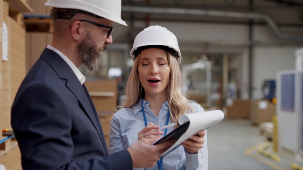 Female warehouse manager talking with logistics employee in warehouse, planning transport of products, goods, talking shipping process. Storing products and materials in warehouse.