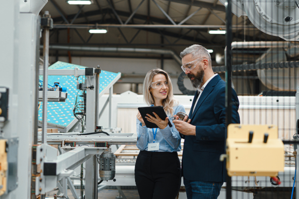 Female engineer and male project manager standing in modern industrial factory by precision robotic arm. Robot assembling wooden furniture in furniture manufacturing facility with industrial robotic manipulators.