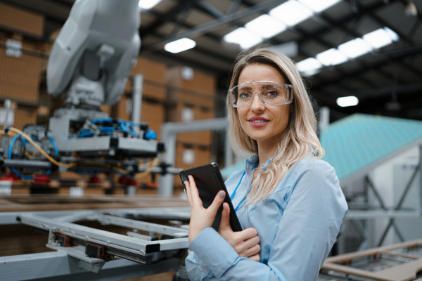 Portrait of female engineer standing in modern industrial factory. Manufacturing facility with robotics and automation. Female leader, CEO in heavy industry, manufactury.