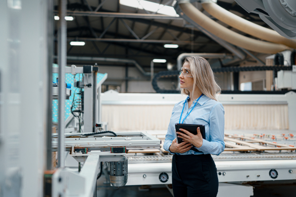 Female engineer in modern industrial factory, checking robotic arm, controling process and manufacturing equipment or machinery. Quality assurance inspectors in manufacturing facility with robotics and automation.