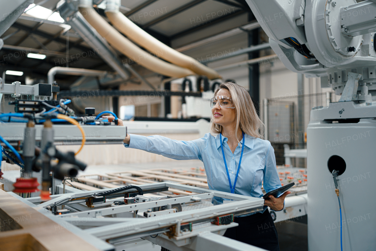 Female engineer in modern industrial factory, checking robotic arm, controling process and manufacturing equipment or machinery. Quality assurance inspectors in manufacturing facility with robotics and automation.