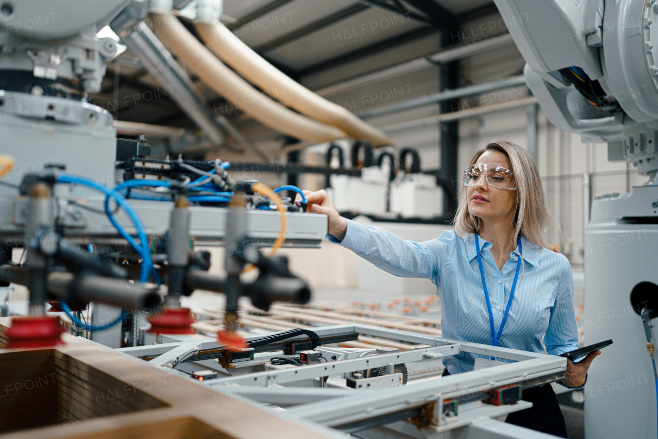 Female engineer in modern industrial factory, checking robotic arm, controling process and manufacturing equipment or machinery. Quality assurance inspectors in manufacturing facility with robotics and automation.