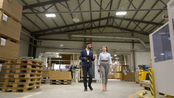 Female warehouse manager talking with logistics employee in warehouse, planning transport of products, goods, talking shipping process. Storing products and materials in warehouse.