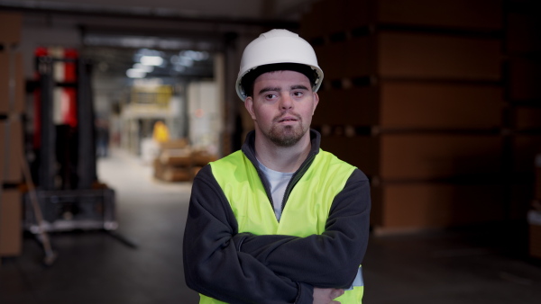 Young man with Down syndrome working in industrial factory, warehouse. Concept of workers with disabilities, support in workplace.