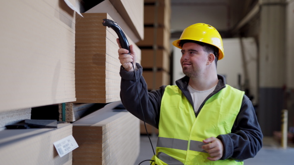 Young man with Down syndrome working in warehouse. Concept of workers with disabilities, support in workplace.