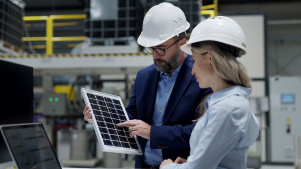 Female engineer and male director talking in modern industrial factory about solar panels installation, solar energy for company. Team management in manufacturing facility. using green renewable energy for business.