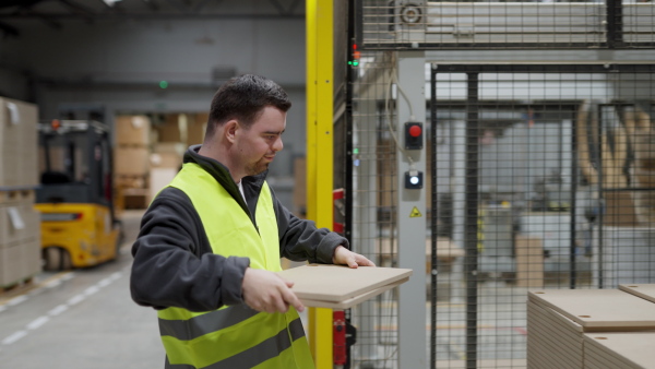 Young man with Down syndrome working in warehouse. Concept of workers with disabilities, support in workplace.