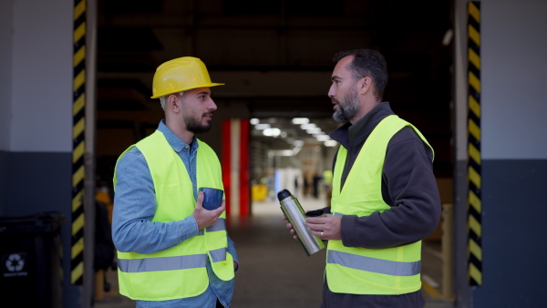 Video of two workers taking break from work, drinking coffee, talking and resting, standing on loading dock, outdoors. Collegues drinking warm tea from thermos. Concept of colleagues friendship.