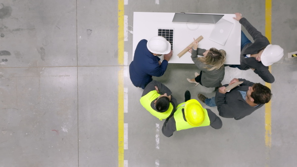 A top view of team of engineers and foremans consulting with director in modern industrial factory, talking about new production project or investment. Team management in manufacturing facility.