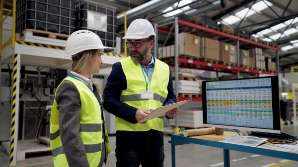 Rear view of female engineer and male supervisor standing in modern industrial factory, talking about production. Team management in manufacturing facility