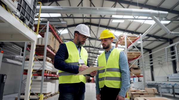 Engineer consulting with product manager in modern industrial factory, explaining new production project or investment, holding product. Team management in manufacturing facility.