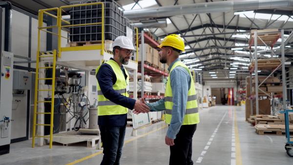 Engineers shaking hands with project manager in modern industrial factory, talking about new production project, investment. Team management in manufacturing facility.