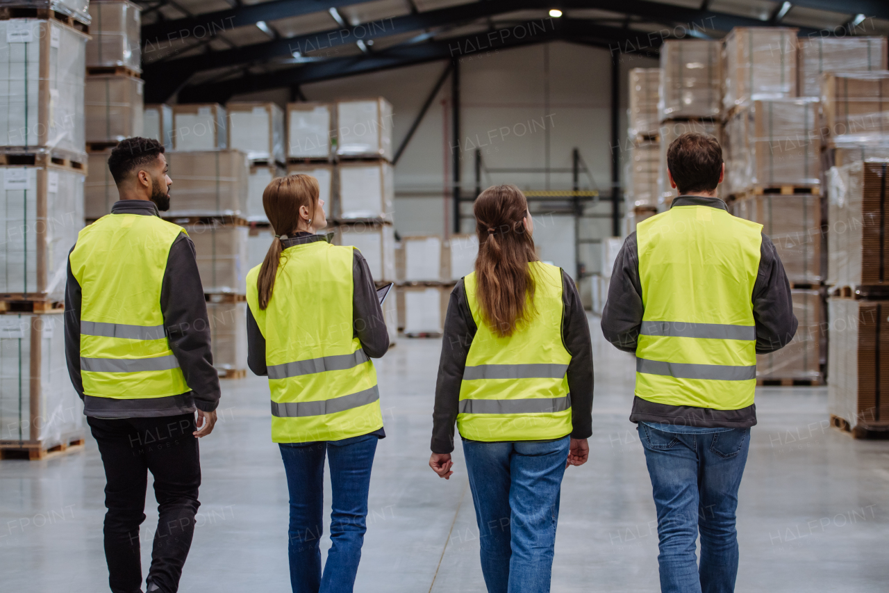 Rear view of warehouse workers in reflective vest walking in warehouse. Team of warehouse workers preparing products for shipment.