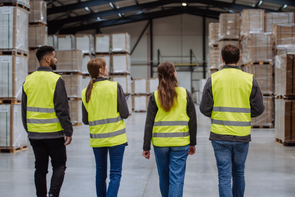 Rear view of warehouse workers in reflective vest walking in warehouse. Team of warehouse workers preparing products for shipment.