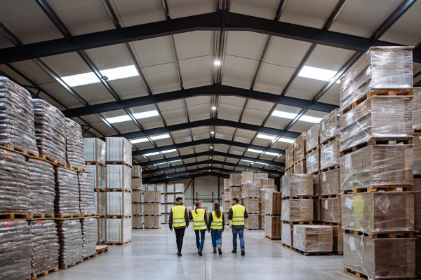 Rear view of warehouse workers in reflective vest walking in warehouse. Team of warehouse workers preparing products for shipment.