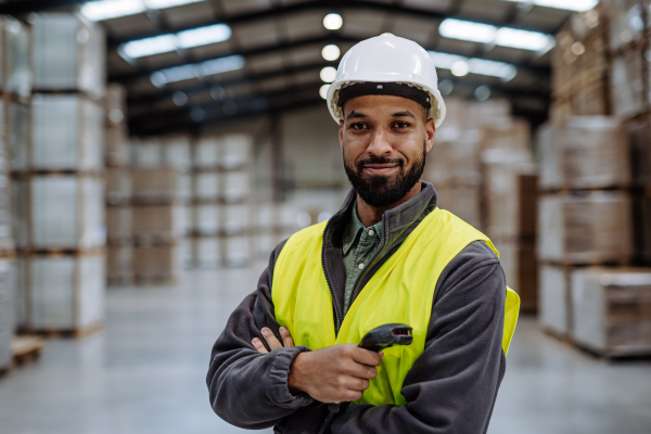 Portrait of warehouseman with scanner, scanning stock in warehouse. Warehouse manager using warehouse management software, app.