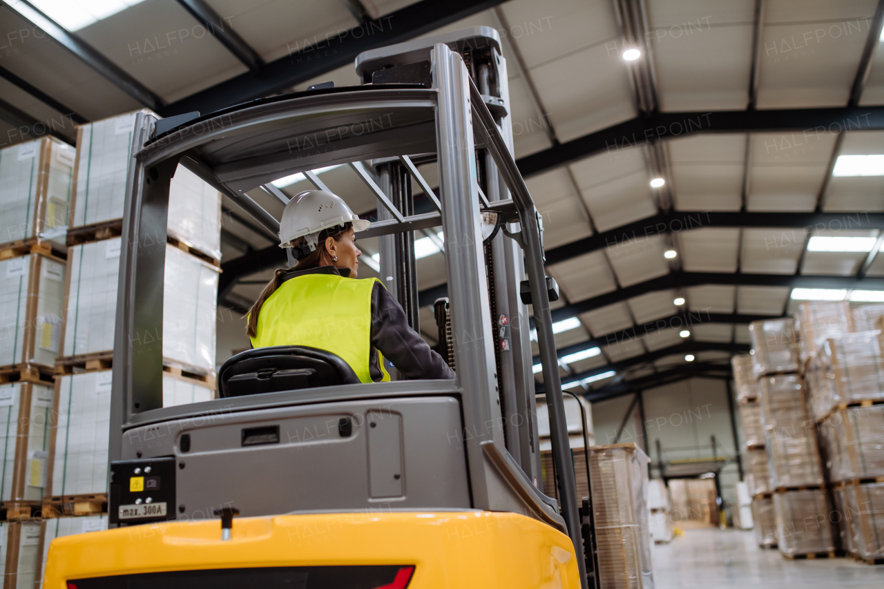 Portrait of female warehouse worker driving forklift. Warehouse worker preparing products for shipmennt, delivery, checking stock in warehouse.