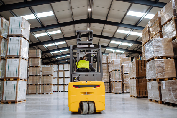 Portrait of female warehouse worker driving forklift. Warehouse worker picking and preparing products for shipmennt, delivery, checking stock in warehouse.