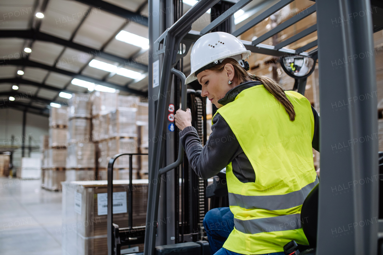 Portrait of female warehouse worker driving forklift. Warehouse worker preparing products for shipmennt, delivery, checking stock in warehouse.