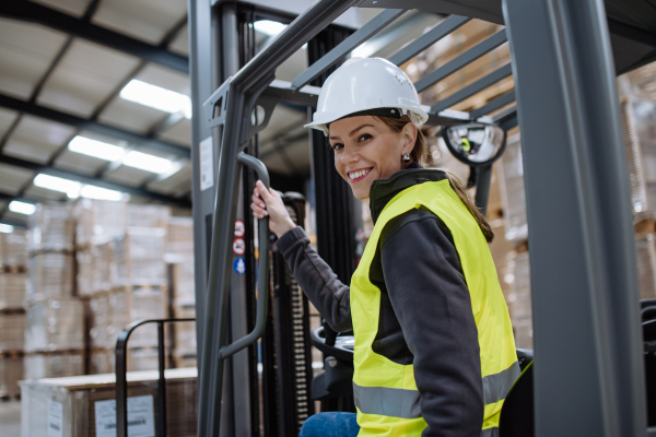 Portrait of female warehouse worker driving forklift. Warehouse worker preparing products for shipmennt, delivery, checking stock in warehouse. Banner with copy space.