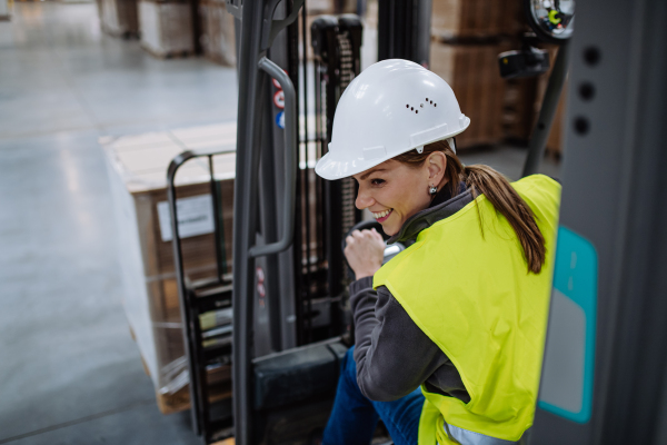 Portrait of female warehouse worker driving forklift. Warehouse worker preparing products for shipmennt, delivery, checking stock in warehouse.