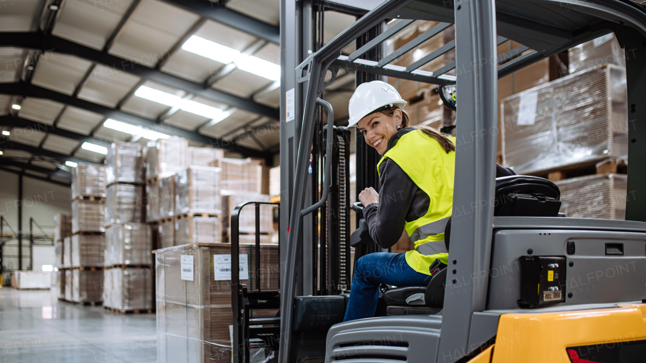 Portrait of female warehouse worker driving forklift. Warehouse worker preparing products for shipmennt, delivery, checking stock in warehouse. Banner with copy space.