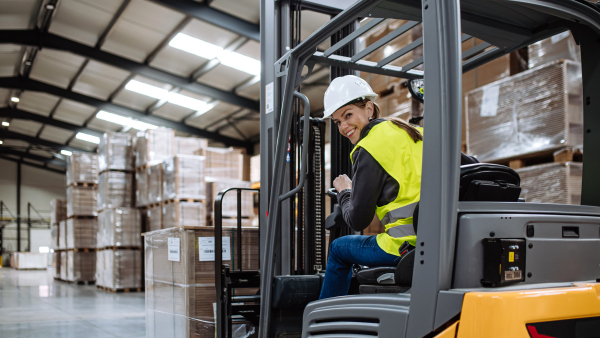 Portrait of female warehouse worker driving forklift. Warehouse worker preparing products for shipmennt, delivery, checking stock in warehouse. Banner with copy space.