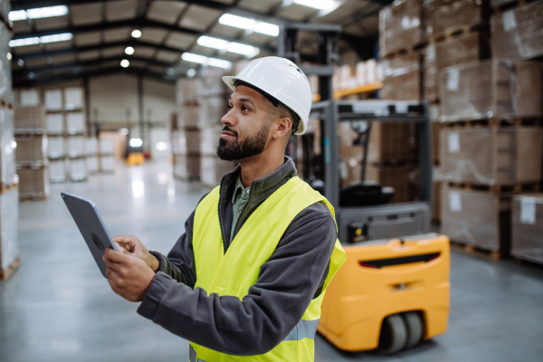 Portrait of warehouseman with tablet checking delivery, stock in warehouse. Warehouse manager using warehouse management software, app.