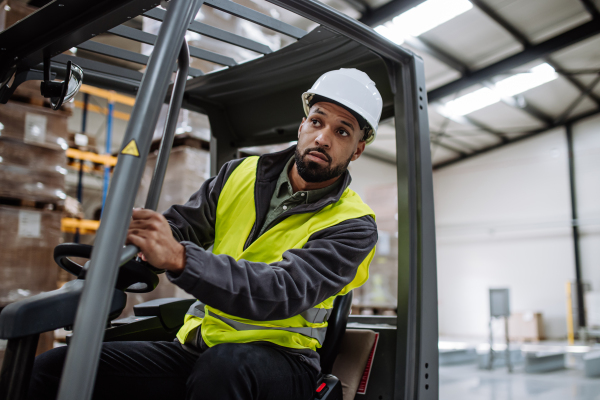 Portrait of multiracial warehouse worker driving forklift. Warehouse worker preparing products for shipmennt, delivery, checking stock in warehouse.