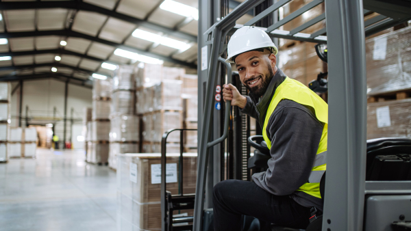 Portrait of multiracial warehouse worker driving forklift. Warehouse worker preparing products for shipmennt, delivery, checking stock in warehouse. Banner with copy space.