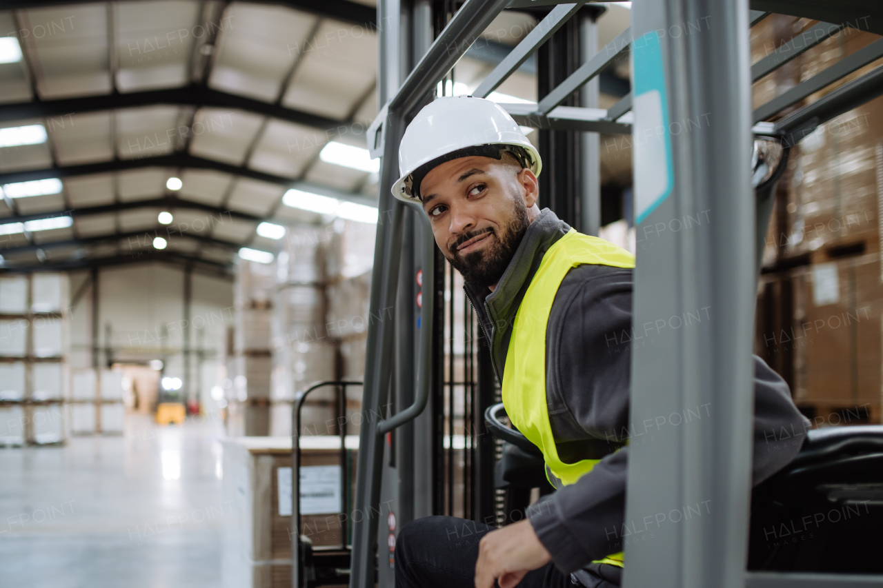 Portrait of multiracial warehouse worker driving forklift. Warehouse worker preparing products for shipmennt, delivery, checking stock in warehouse.