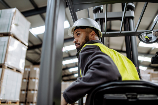 Portrait of multiracial warehouse worker driving forklift. Warehouse worker preparing products for shipmennt, delivery, checking stock in warehouse.