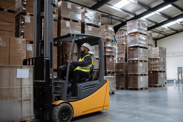 Portrait of multiracial warehouse worker driving forklift. Warehouse worker preparing products for shipmennt, delivery, checking stock in warehouse.