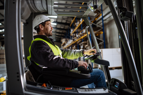 Portrait of multiracial warehouse worker driving forklift. Warehouse worker preparing products for shipmennt, delivery, checking stock in warehouse.