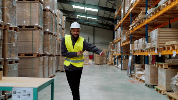 Warehouseman with tablet helmet dancing in the middle of the warehouse. Warehouse working having fun at work.