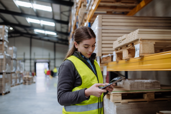 Female warehouse worker holding scanner and scanning the barcodes on products in warehouse. Warehouse manager using warehouse scanning system.