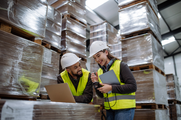 Warehouse manager talking and laughing with logistics employee in warehouse, planning transport of products, goods, talking shipping process. Concept of good work relationship.