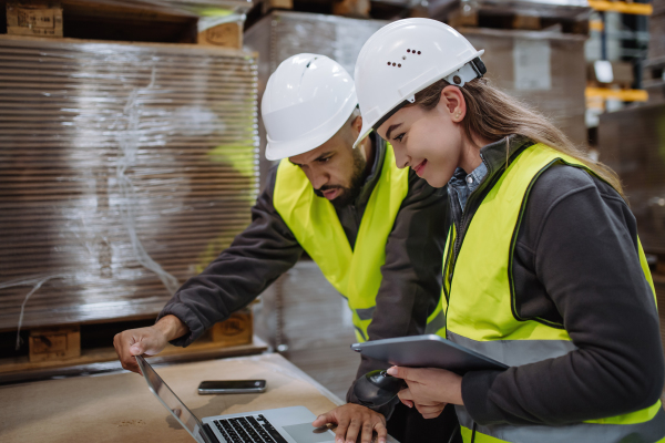 Warehouse manager talking with logistics employee in warehouse, planning transport of products, goods, talking shipping process.