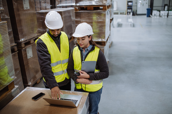 Warehouse manager talking with logistics employee in warehouse, planning transport of products, goods, talking shipping process.