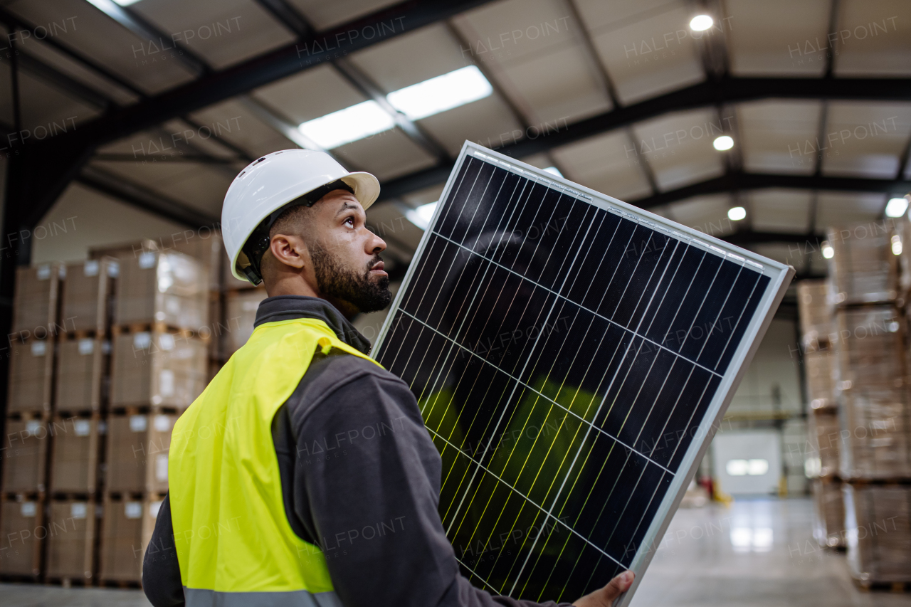 Handsome worker carrying solar panel in warehouse or factory. Solar panel manufacturer, solar manufacturing.