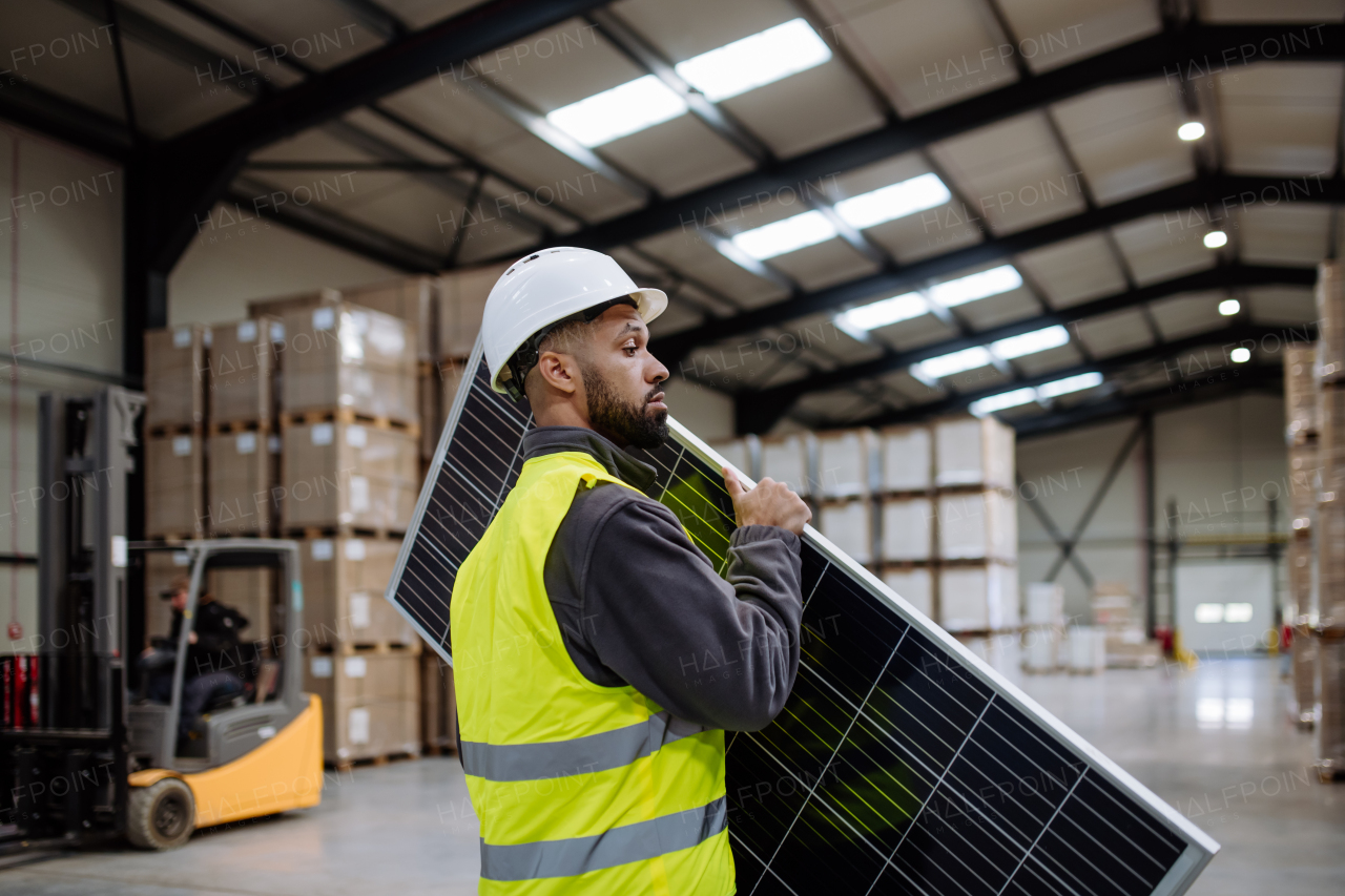 Handsome worker carrying solar panel in warehouse or factory. Solar panel manufacturer, solar manufacturing.